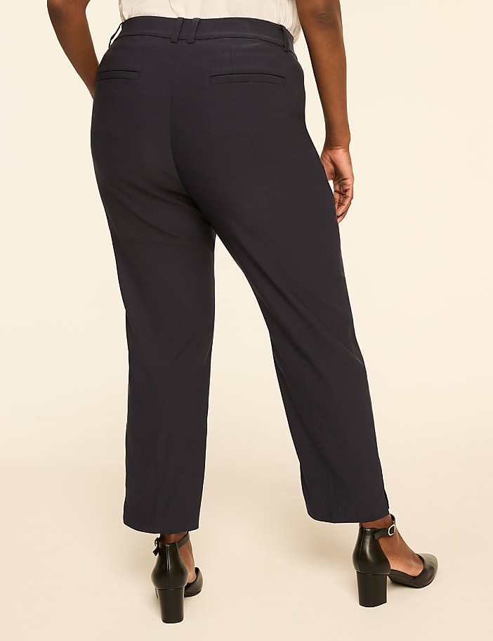 A person wearing dark blue pants and black heels stands against a plain, light-colored background.