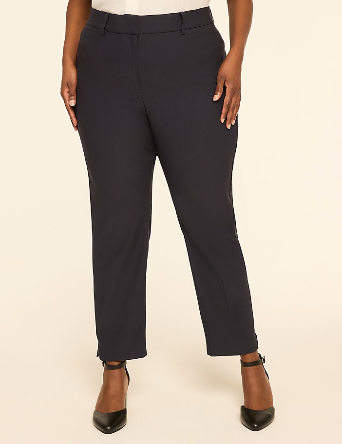 A person stands in dark dress pants and black heels against a plain, light-colored background.