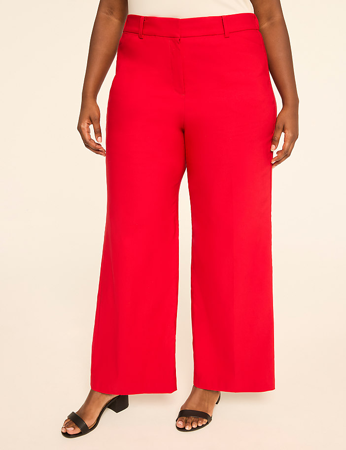 A person stands in bright red wide-leg pants and black sandals against a plain, light-colored background.