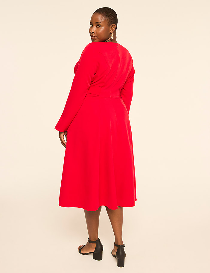 A woman in a red dress stands against a plain, light-colored background.