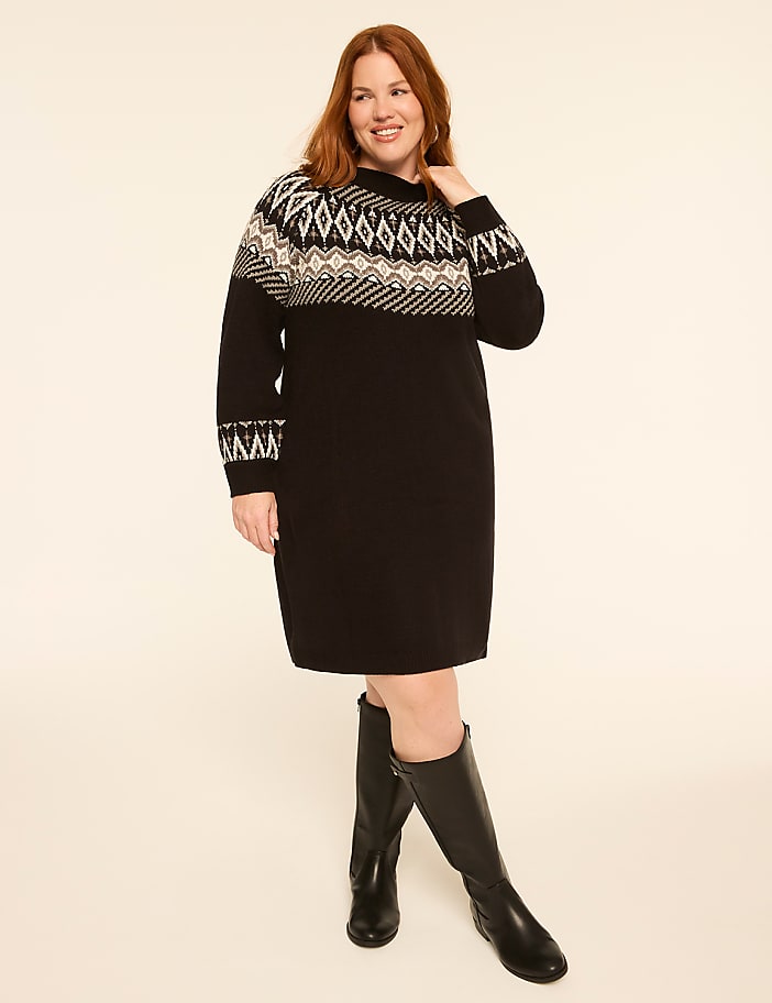 A woman in a black dress with a fair isle pattern stands against a plain, light-colored background.