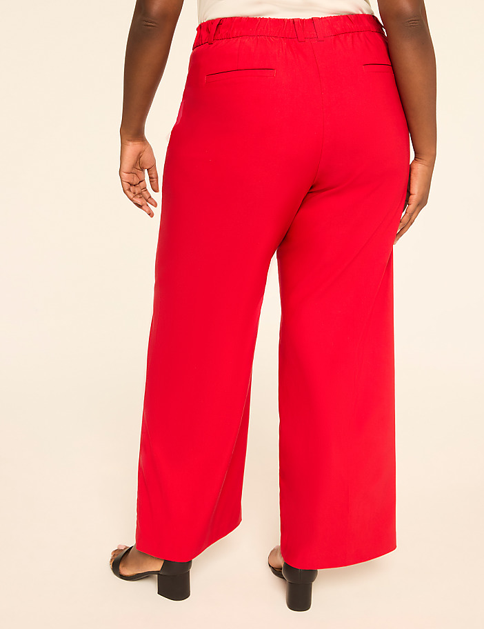 A person wearing red wide-leg pants stands against a plain, light-colored background.