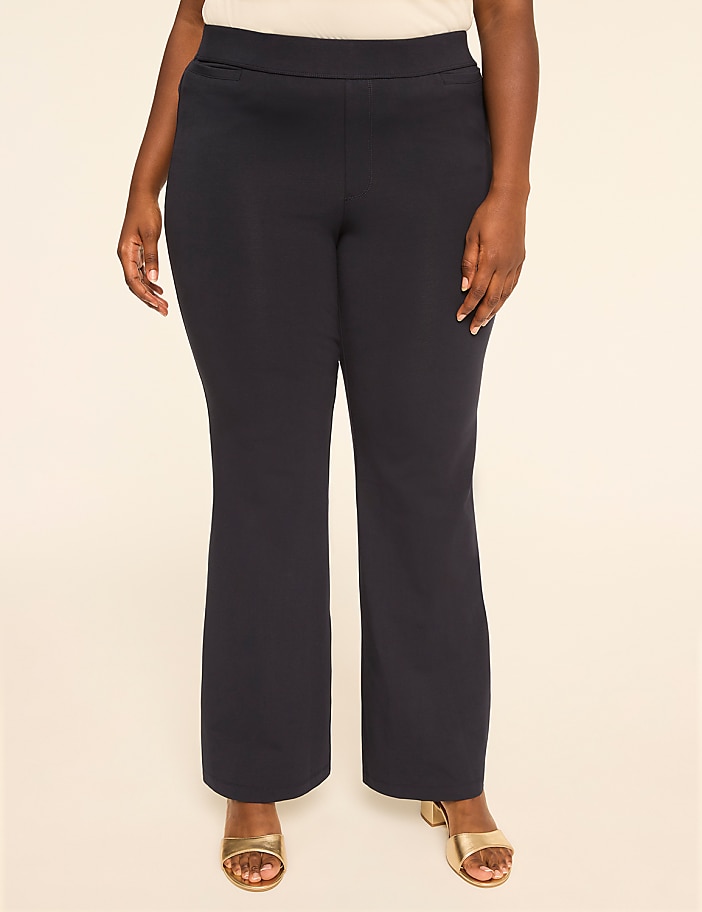 A woman in dark flared pants and gold heels stands against a plain, light-colored background.