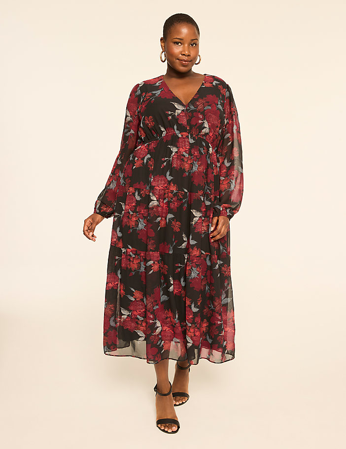 A woman in a floral dress stands against a plain, light-colored background.
