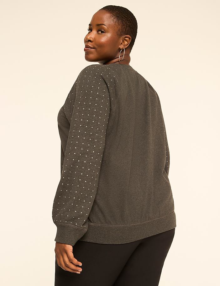 A woman in a dark, textured sweater with silver polka dots on the sleeves stands against a plain, light-colored background.