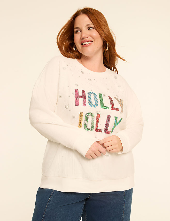 A woman in a cream-colored sweatshirt with "HOLLY JOLLY" in colorful sequins stands against a plain, light-colored background.