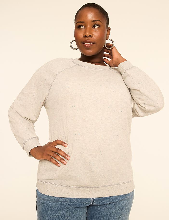 A woman in a light gray sweatshirt and blue jeans poses against a plain, light-colored background.