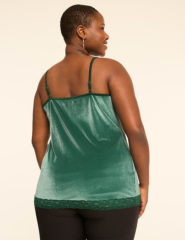 A woman in a green velvet camisole with lace trim stands against a plain, light-colored background.