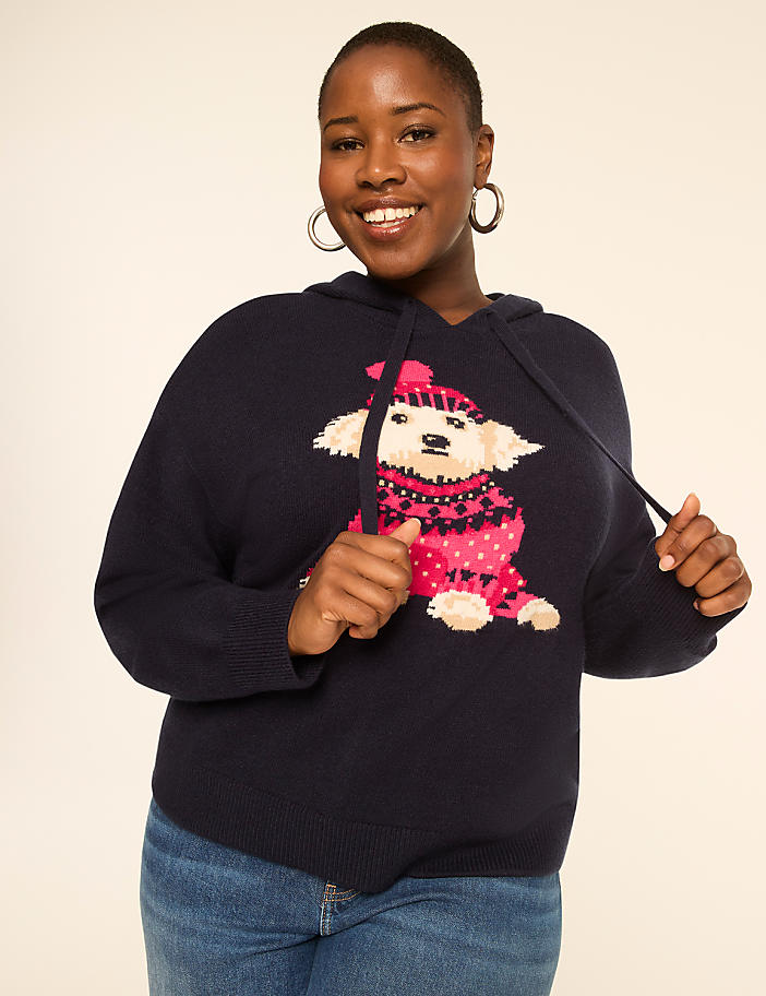 A smiling woman in a navy hoodie with a dog graphic stands against a plain, light-colored background.