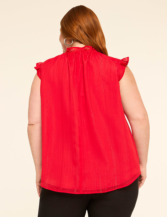 A woman with red hair wearing a red ruffled blouse stands against a plain beige background.