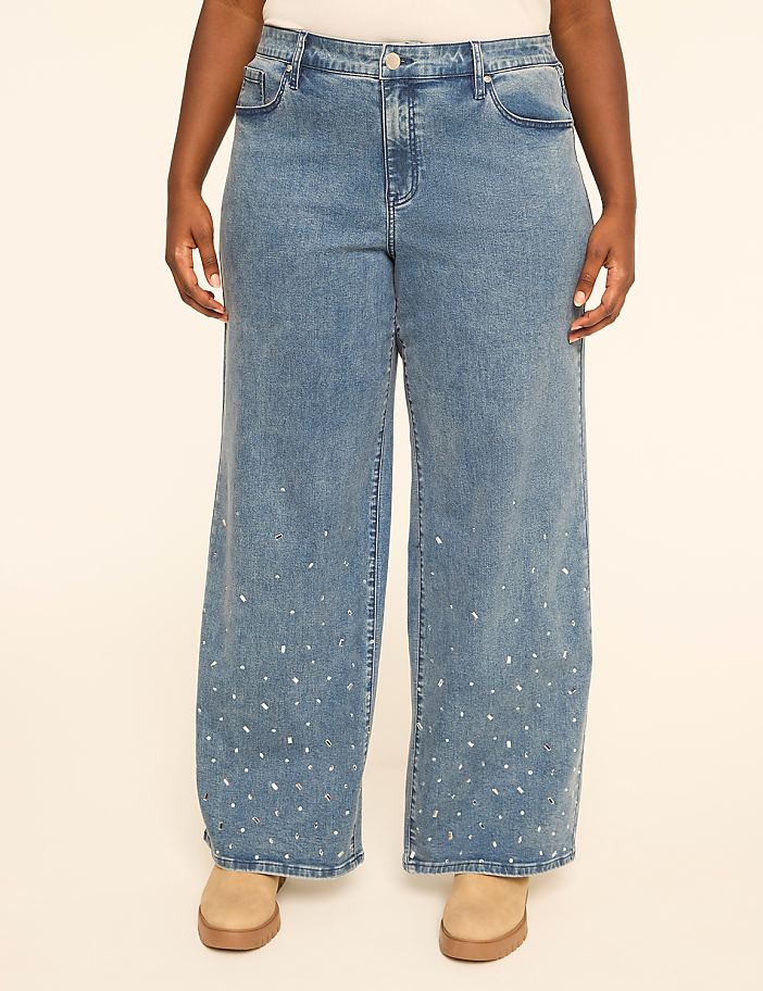 A person stands in light-wash wide-leg jeans adorned with scattered rhinestones, against a plain beige background.
