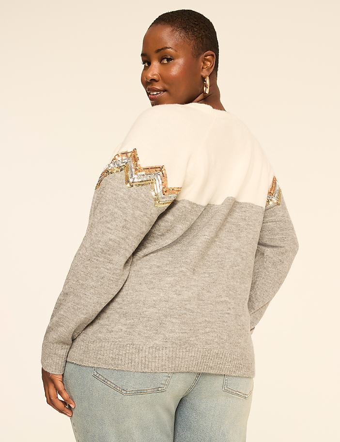 A woman in a light gray and white sweater with sequined accents poses against a plain, light-colored background.