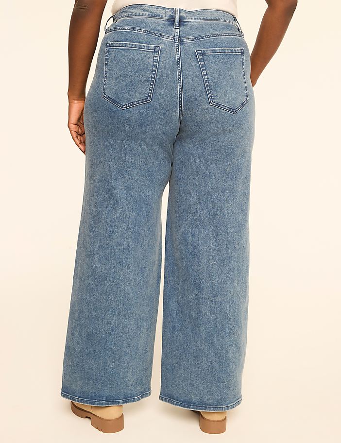 A person wearing wide-leg blue jeans stands against a plain, light-colored background.