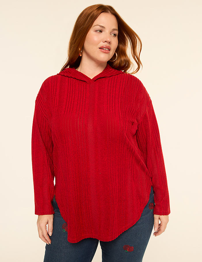 A woman with red hair and a red hoodie stands against a plain, light-colored background.