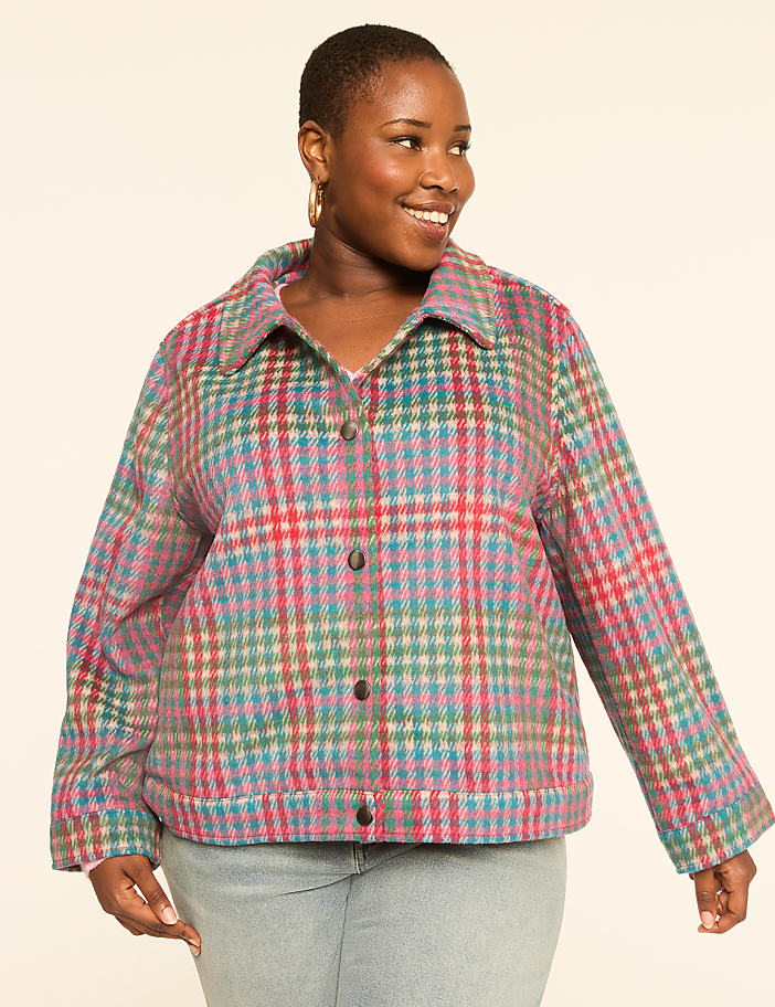 A smiling woman in a colorful plaid jacket stands against a plain, light background.