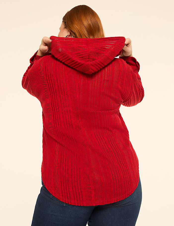 A woman in a red hooded shirt stands against a plain, light-colored background.