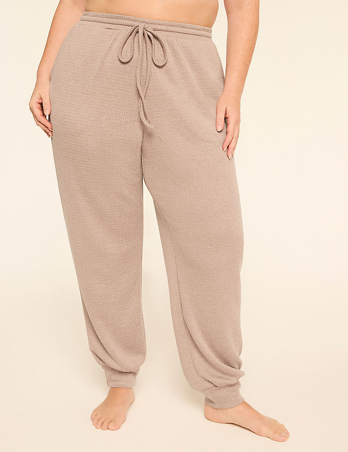 A person stands in the foreground wearing beige waffle-knit sweatpants with a drawstring, against a plain, light-colored background.