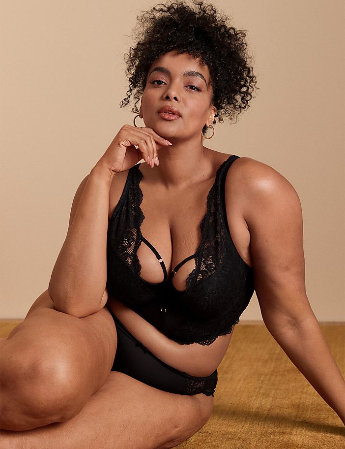 A woman in black lingerie poses on a textured yellow surface with a plain beige background.