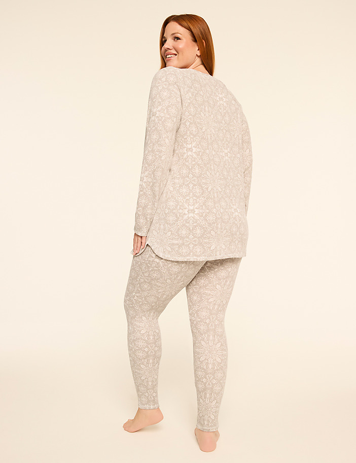 A woman in patterned pajamas stands against a plain, light-colored background.