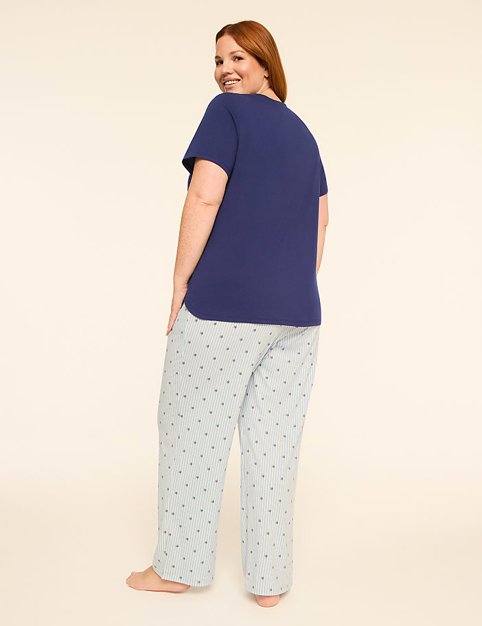 A woman in a navy t-shirt and striped pajama pants stands against a plain, light-colored background.