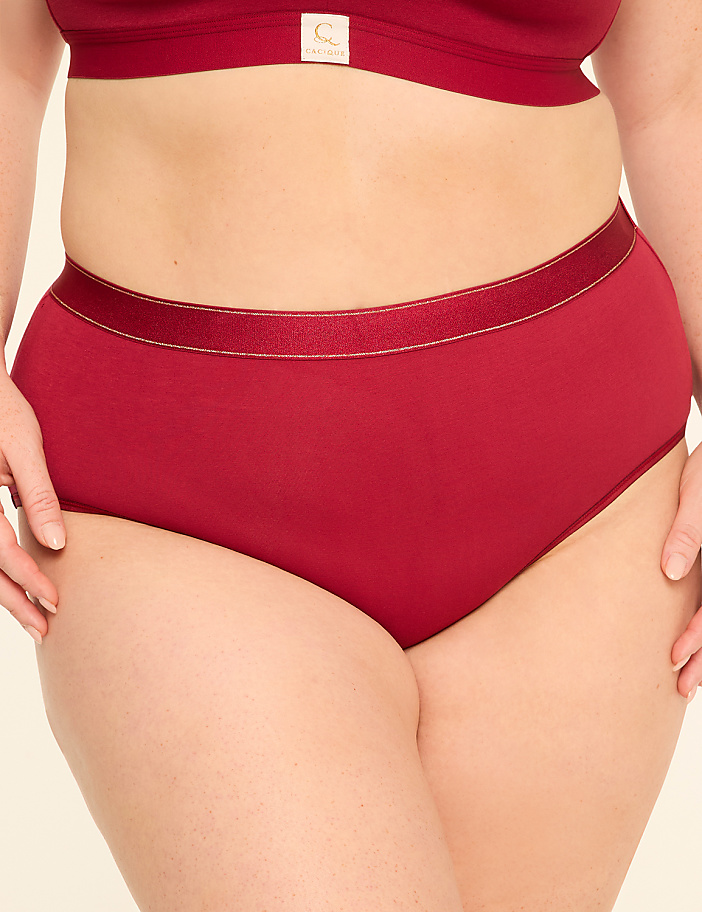 A person wears a red bra and matching high-waisted underwear against a plain, light-colored background.