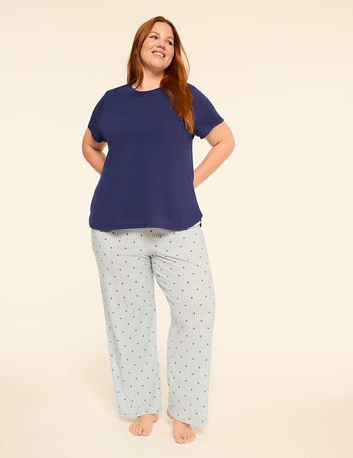 A smiling woman in a navy blue t-shirt and striped pajama pants stands against a plain, light-colored background.