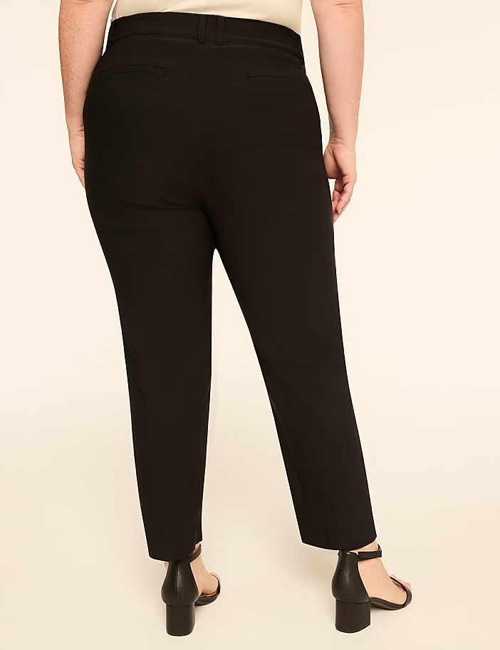 A person wearing black pants and black heels stands against a plain, light-colored background.