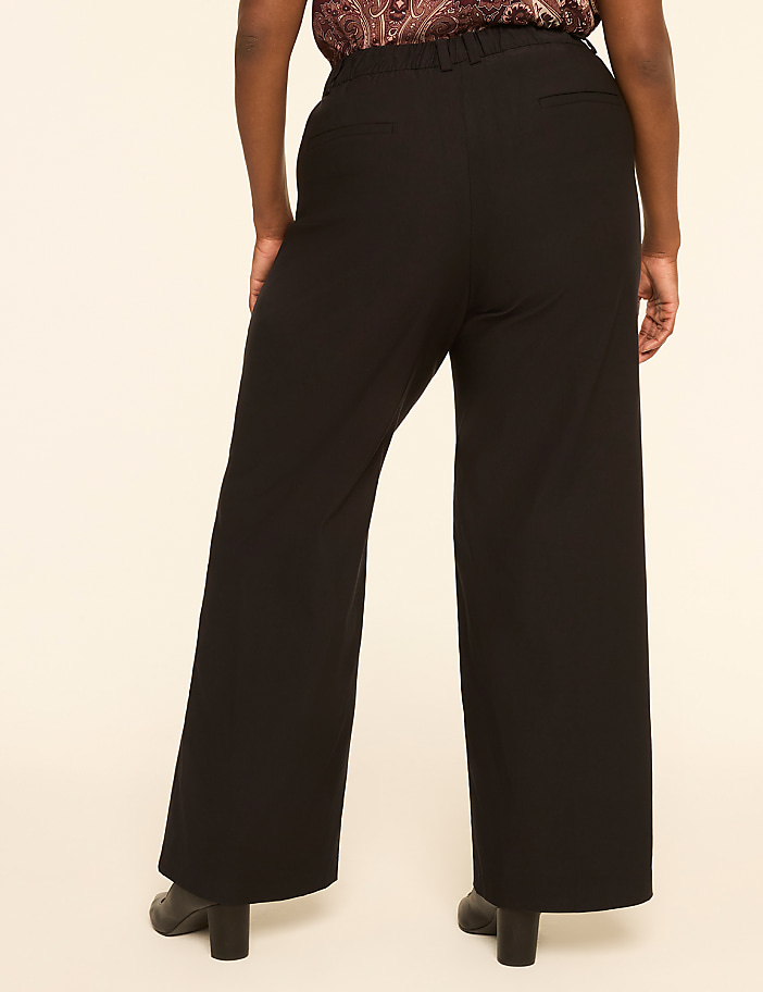 A person wearing black wide-leg pants and black heeled shoes stands against a plain, light-colored background.