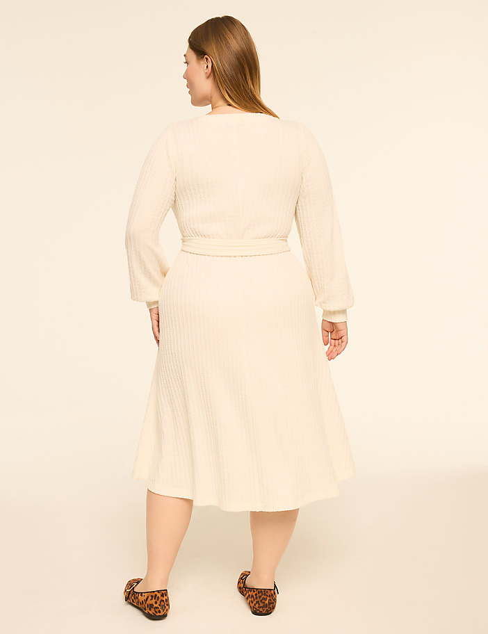 A woman in a cream-colored ribbed dress and leopard print flats stands against a plain, light background.
