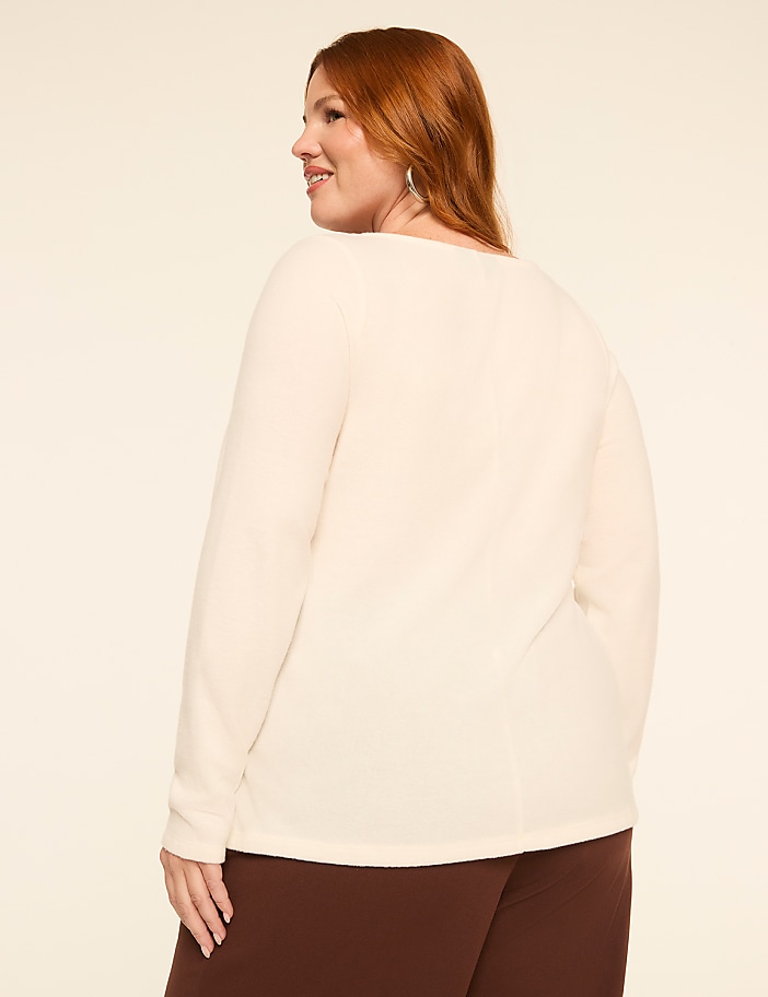 A woman with red hair, wearing a cream-colored waffle-knit top and brown pants, is shown from the back against a plain beige background.