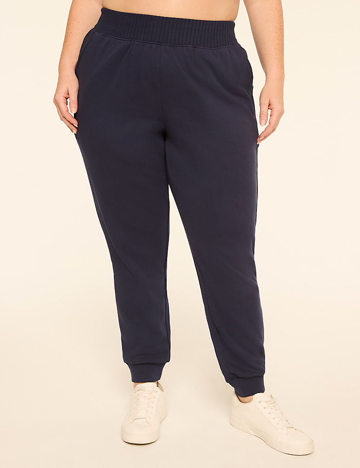 A person in navy blue sweatpants and white sneakers stands against a plain, light-colored background.