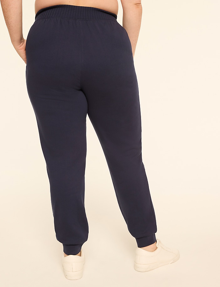 A person wearing navy blue sweatpants and white sneakers stands with their back to the camera against a plain, light-colored background.