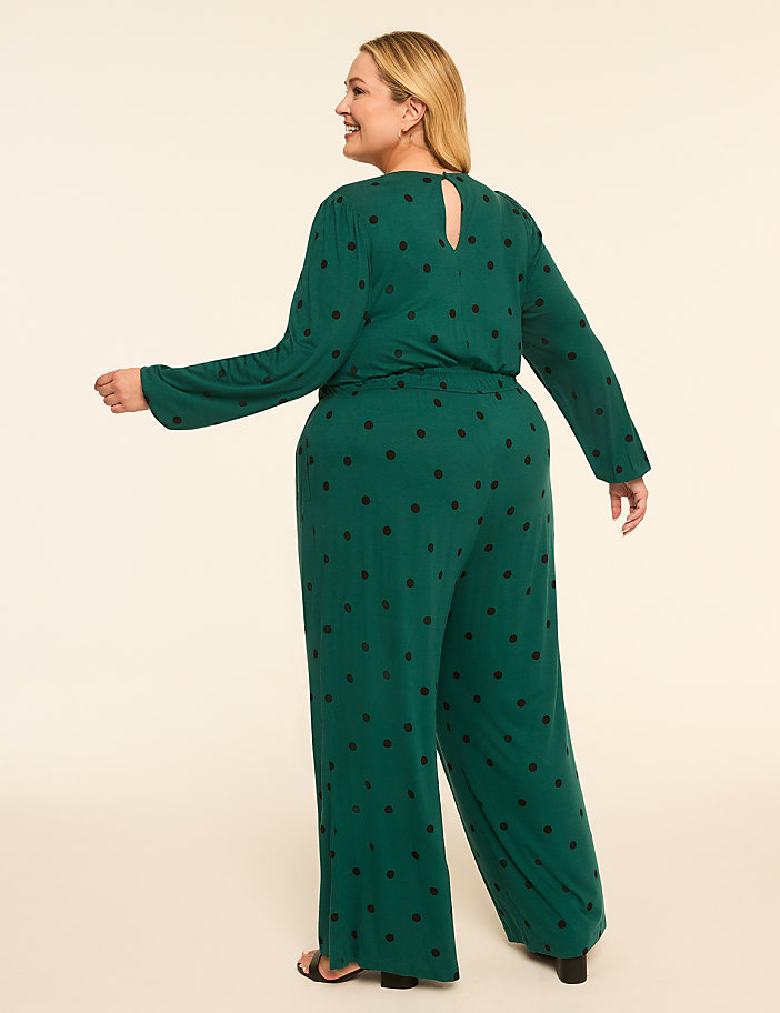 A woman in a green polka-dot jumpsuit poses against a plain, light-colored background.