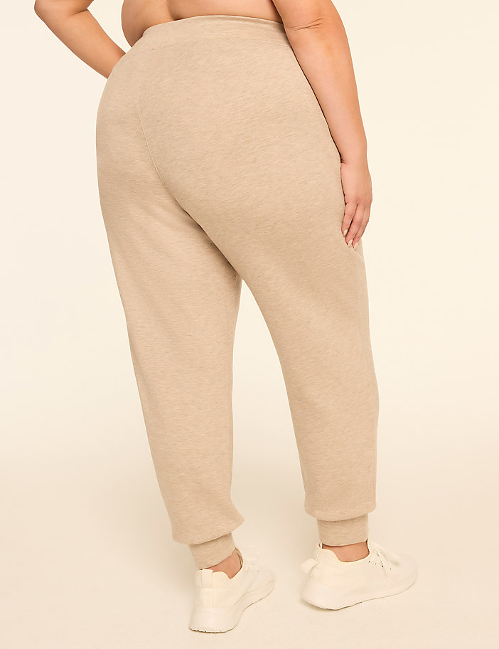 A person wearing beige sweatpants and white sneakers stands against a plain, light-colored background.