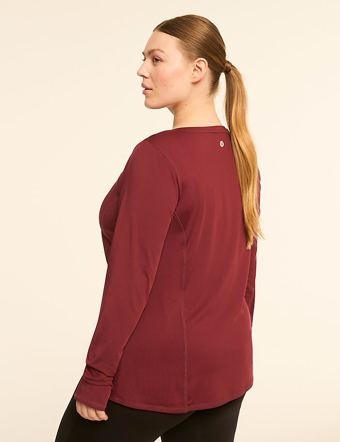 A woman in a maroon long-sleeved shirt and black leggings stands against a plain, light-colored background.