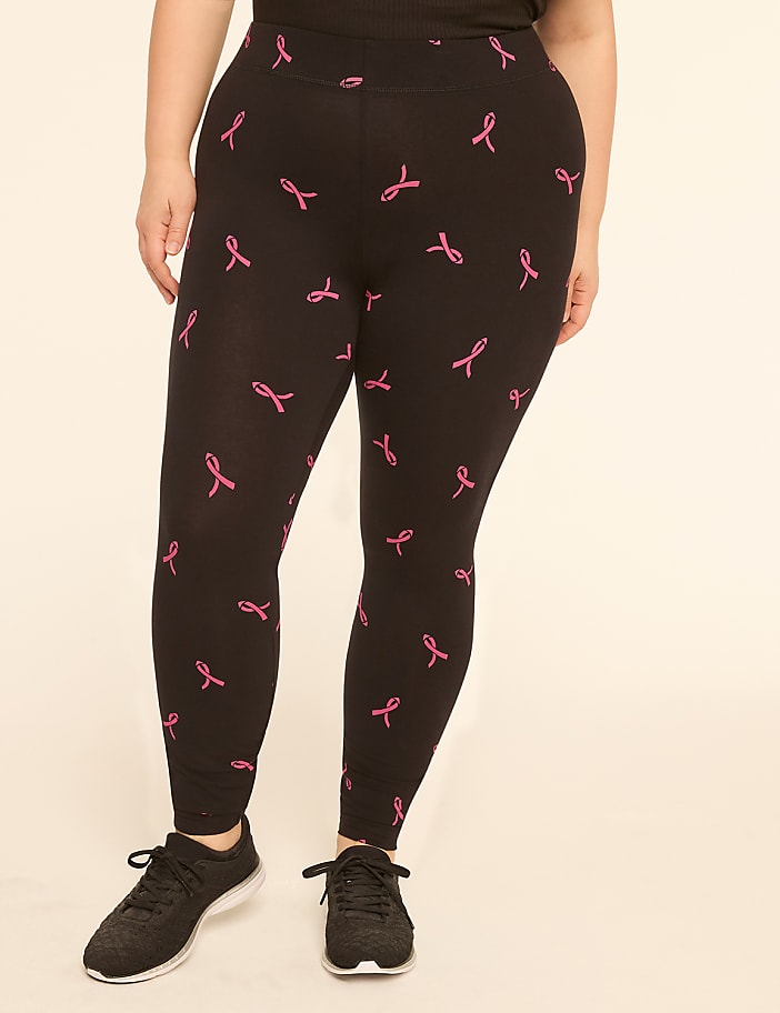 A person wearing black leggings with a pink ribbon pattern stands against a plain, light-colored background.