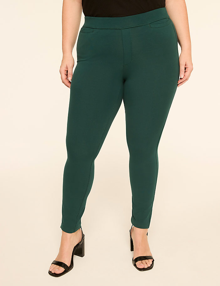 A person wearing dark green leggings and black heels stands against a plain, light-colored background.
