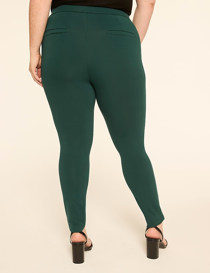 A person wearing dark green pants and black heels stands against a plain beige background.