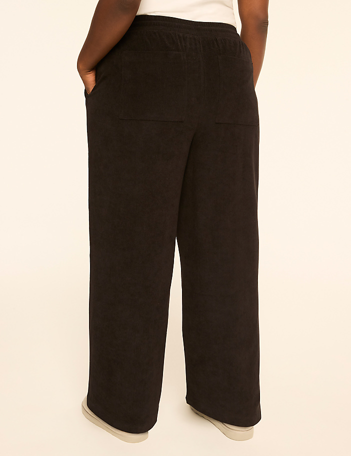 A person wearing black wide-leg pants stands against a plain, light-colored background.