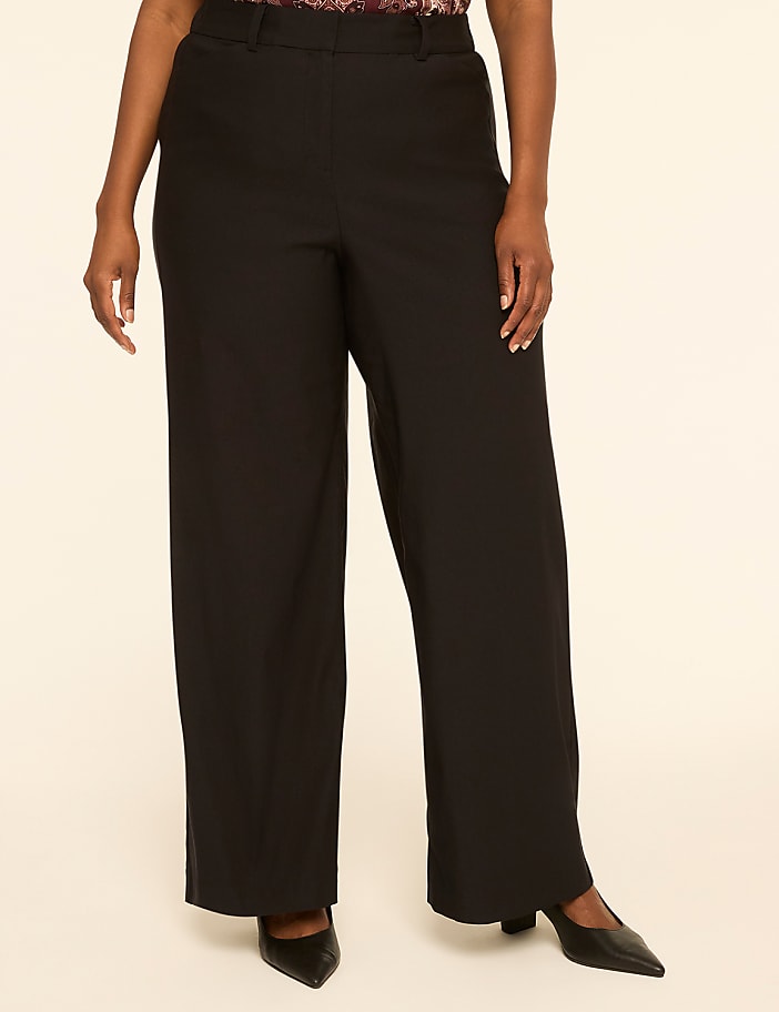 A person stands in black wide-leg pants and pointed-toe heels against a plain, light-colored background.