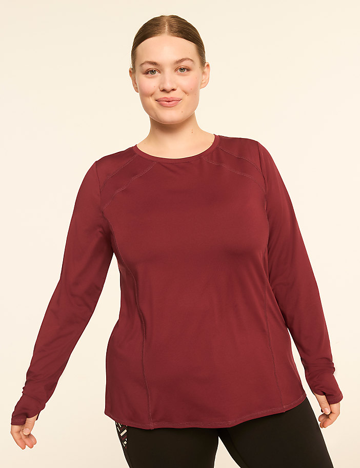 A woman in a maroon long-sleeved shirt and black leggings stands against a plain, light-colored background.