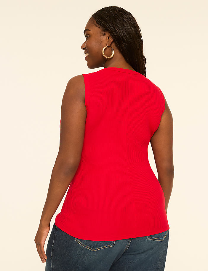 A woman in a red sleeveless top and blue jeans stands against a plain, light-colored background.