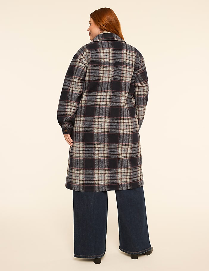 A woman in a plaid coat and wide-leg jeans stands against a plain, light-colored background.