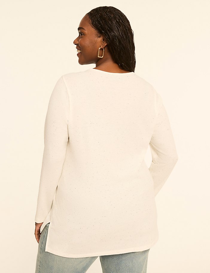 A woman in a white long-sleeved shirt and jeans stands against a plain, light-colored background.
