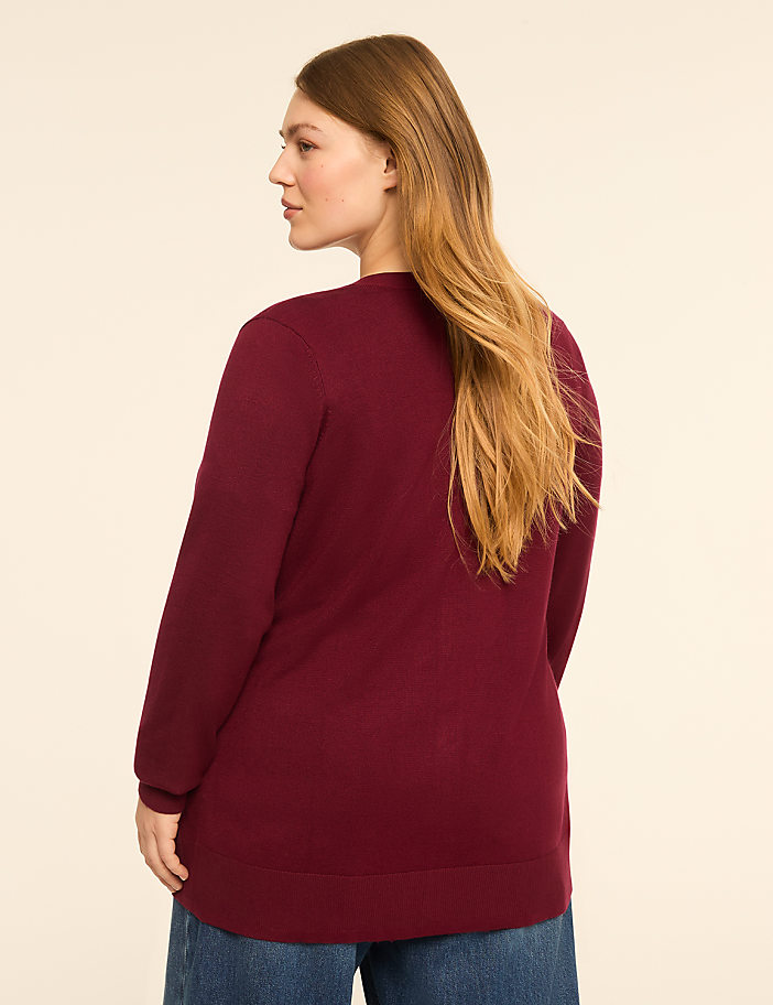 A woman in a maroon sweater and blue jeans stands against a plain, light-colored background.