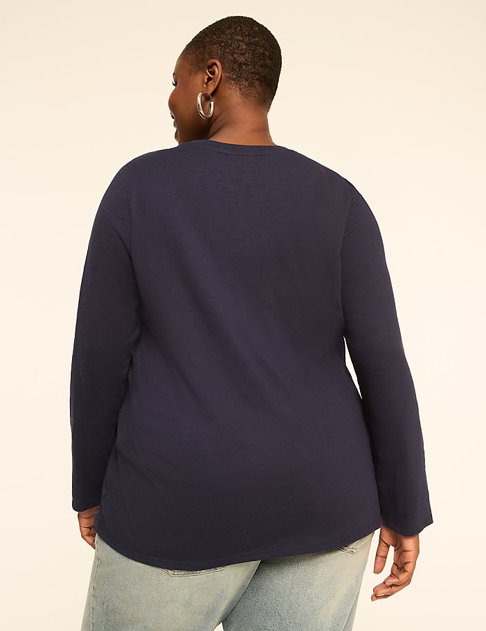 A woman in a navy long-sleeved shirt and light blue jeans stands against a plain, light-colored background.