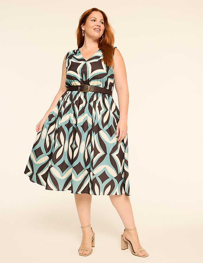 A smiling woman in a patterned dress stands against a plain, light-colored background.