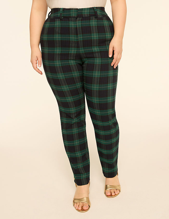 A person stands in the foreground wearing green and black plaid pants and gold sandals, against a plain, light-colored background.