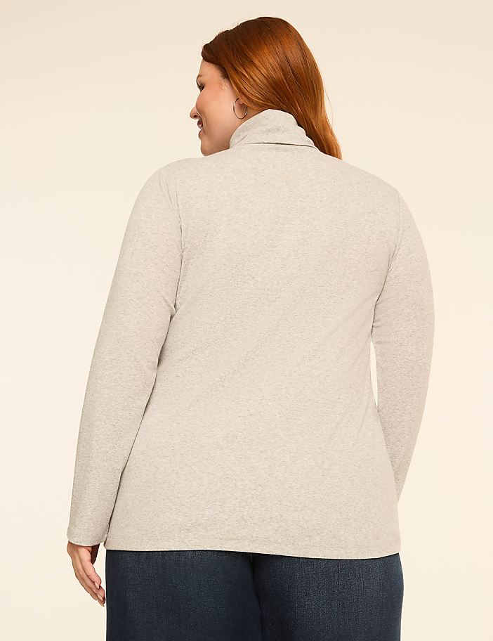 A woman with red hair, seen from the back, wears a light gray turtleneck sweater and dark blue jeans against a plain, light background.