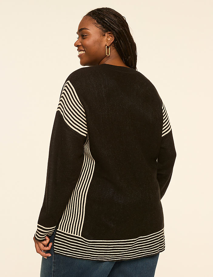 A woman in a striped sweater smiles over her shoulder against a plain, light-colored background.